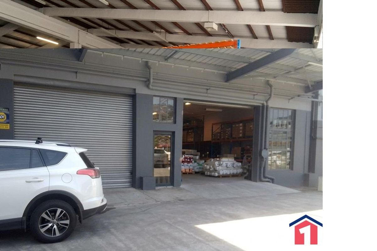 Industrial warehouse exterior featuring a roller shutter door, steel frame construction, and exposed roof trusses, providing functional access for commercial operations.