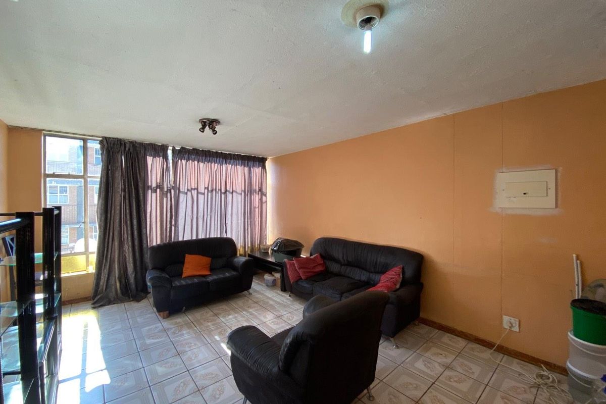A living room featuring tiled flooring, a large window, and an exposed electrical distribution board on the wall.