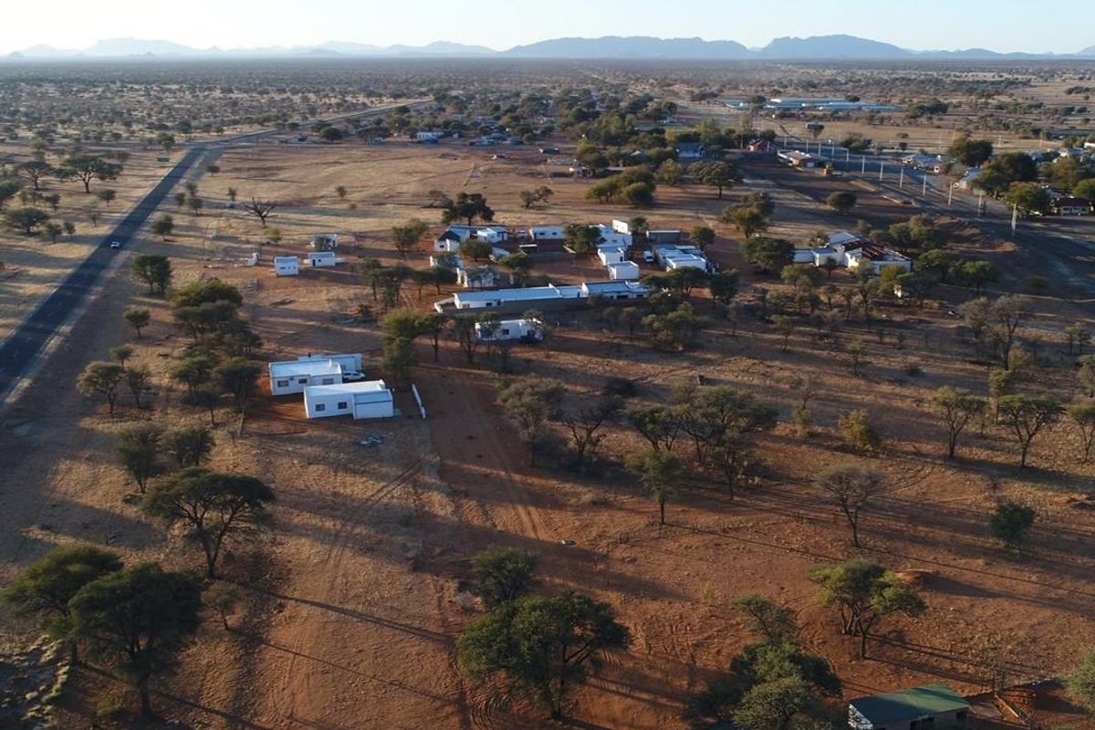 Aerial view of a large residential land plot featuring multiple scattered structures, natural vegetation, and surrounding road access.