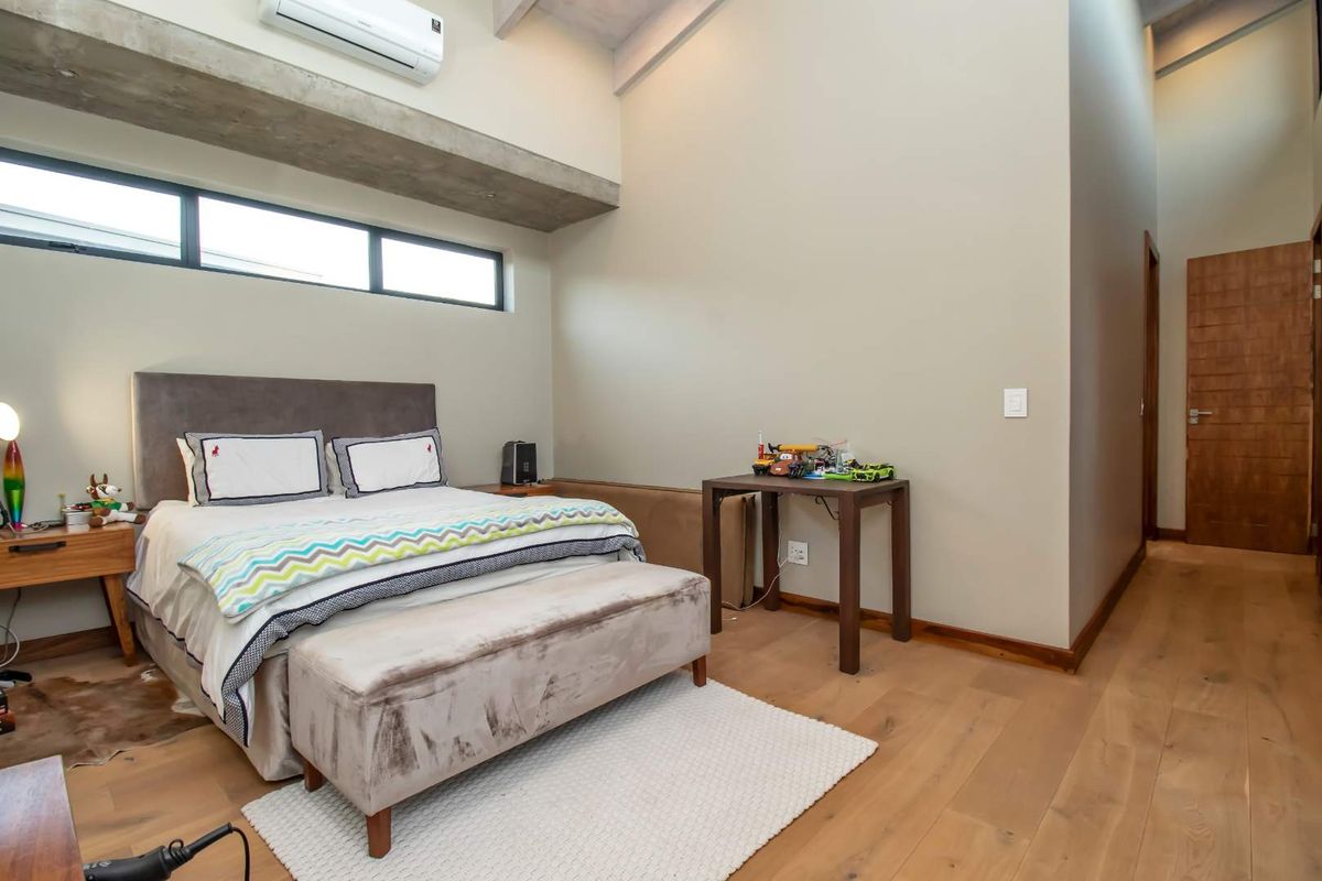 Spacious bedroom featuring high vaulted ceilings, exposed concrete beam, timber flooring, and clerestory windows for natural light.