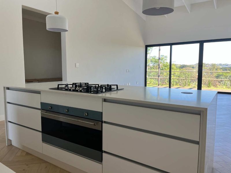 Modern kitchen featuring a central island with built-in gas hob and oven, herringbone flooring, and large sliding doors opening to an outdoor view.