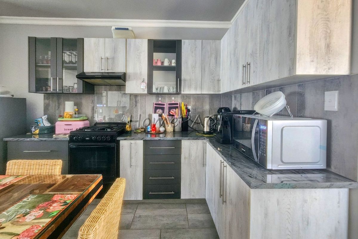 A functional kitchen featuring modern wood-look cabinetry, granite countertops, a gas stove with extractor fan, and durable tiled flooring.