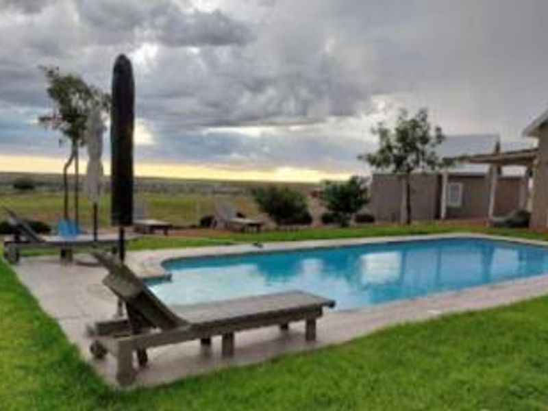 Outdoor swimming pool area with a paved deck and surrounding lawn, set against a scenic rural landscape.