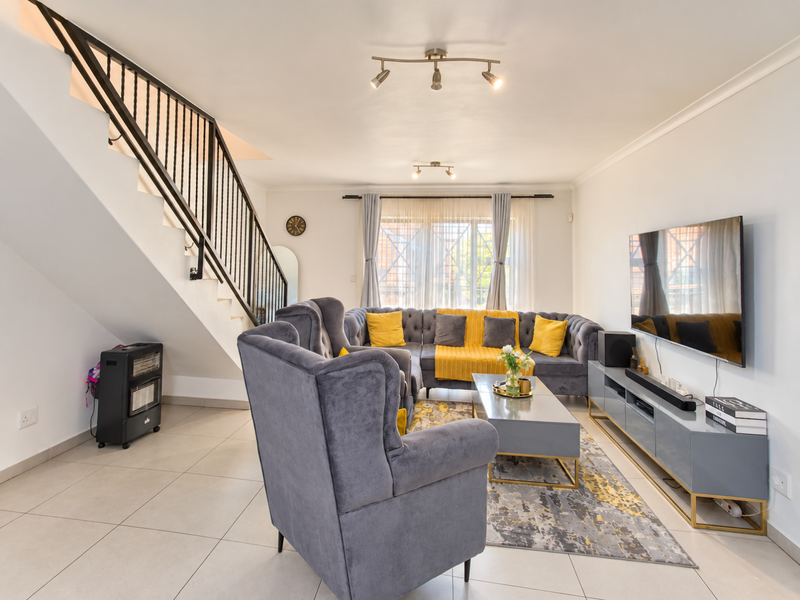 A bright and well-maintained living room featuring tiled flooring, a modern staircase with a metal balustrade, and contemporary track lighting.