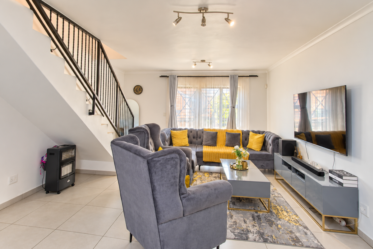 A bright and well-maintained living room featuring tiled flooring, a modern staircase with a metal balustrade, and contemporary track lighting.