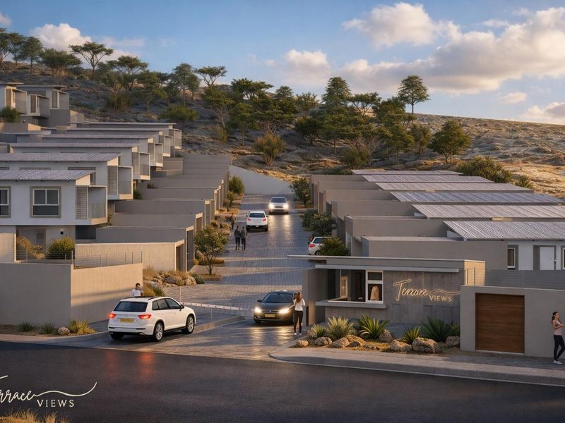 A modern townhouse development entrance featuring a security gatehouse, paved access road, and terraced residential units with solar panel installations.
