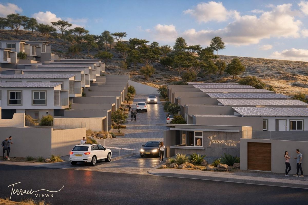 A modern townhouse development entrance featuring a security gatehouse, paved access road, and terraced residential units with solar panel installations.