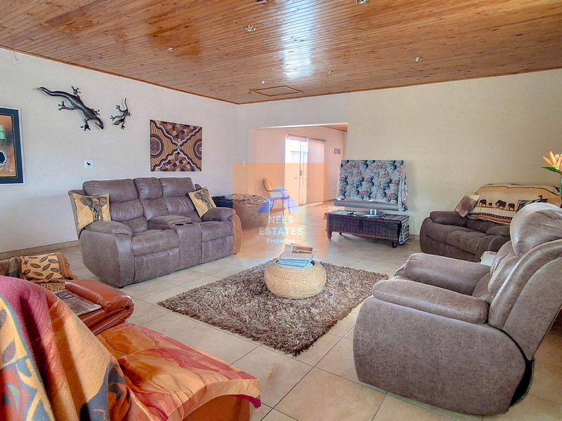 Spacious living room featuring tiled flooring, a timber tongue and groove ceiling with recessed lighting, and a decorative glass block window.