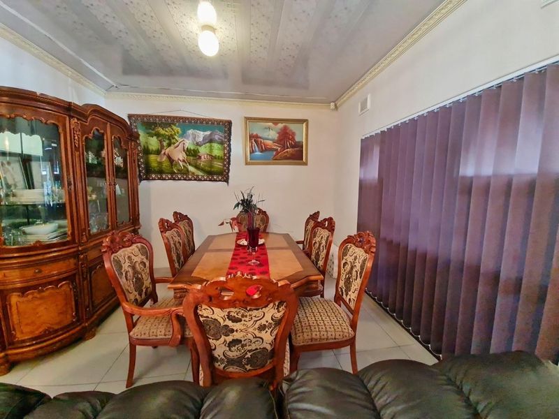 A traditional dining room featuring tiled flooring, decorative ceiling cornicing, and vertical window blinds, providing a functional space for family meals.