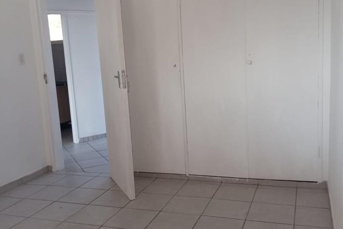 An empty bedroom featuring neutral tiled flooring and built-in cupboards, offering a clean and versatile space ready for personalization.