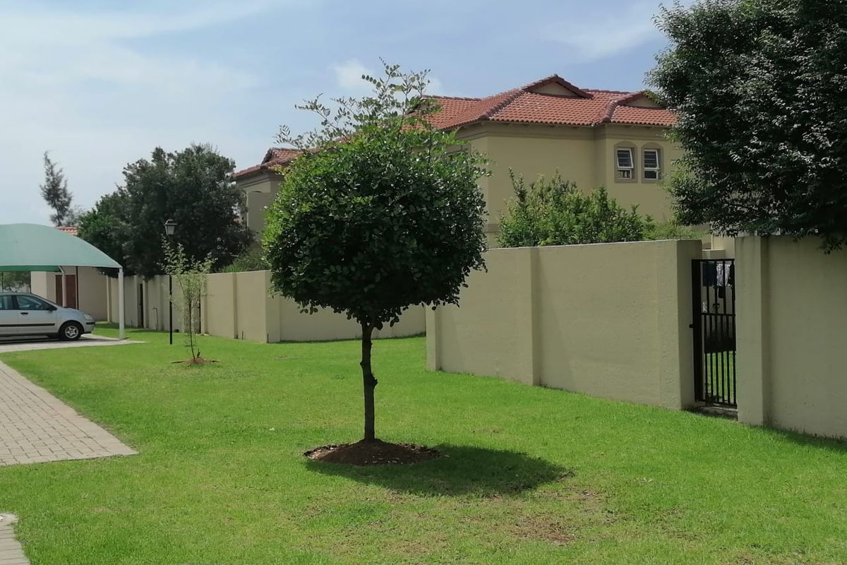 A view of the rear exterior area featuring a well-maintained lawn, boundary walls, and a paved walkway leading to the apartment complex.