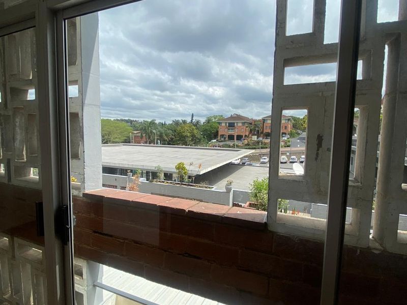 A view from an apartment window featuring a decorative concrete screen and brick sill, overlooking the surrounding neighbourhood and parking area.