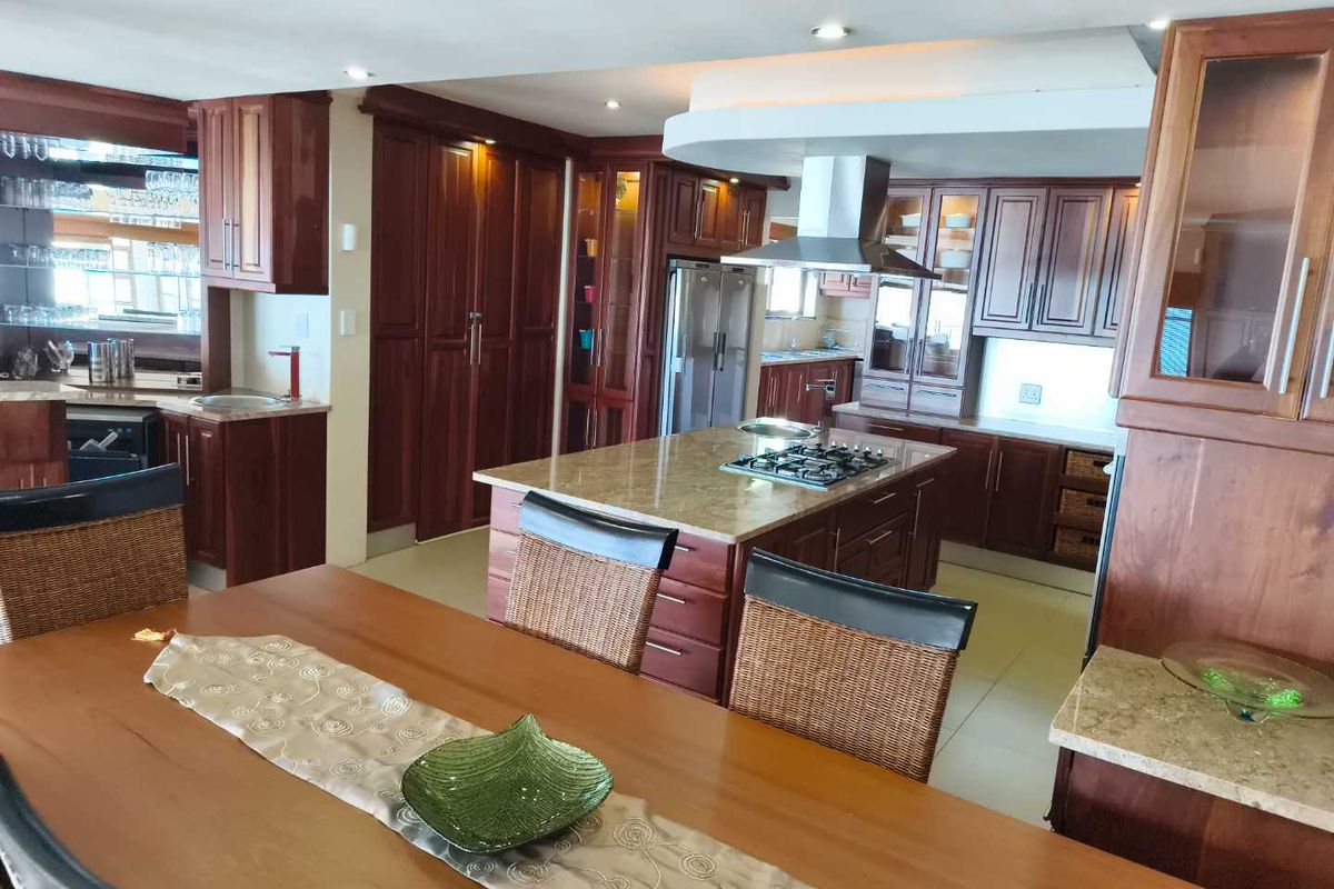 Spacious kitchen featuring extensive dark wood cabinetry, granite countertops, a central island with a gas hob, and integrated stainless steel appliances.