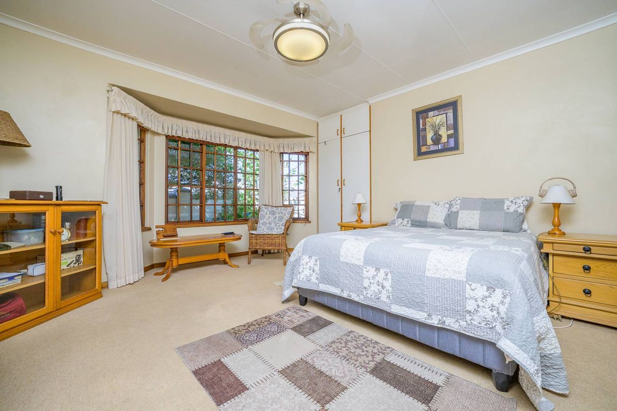 A well-lit bedroom featuring a large bay window, built-in cupboards, and a ceiling fan, offering a comfortable and functional living space.
