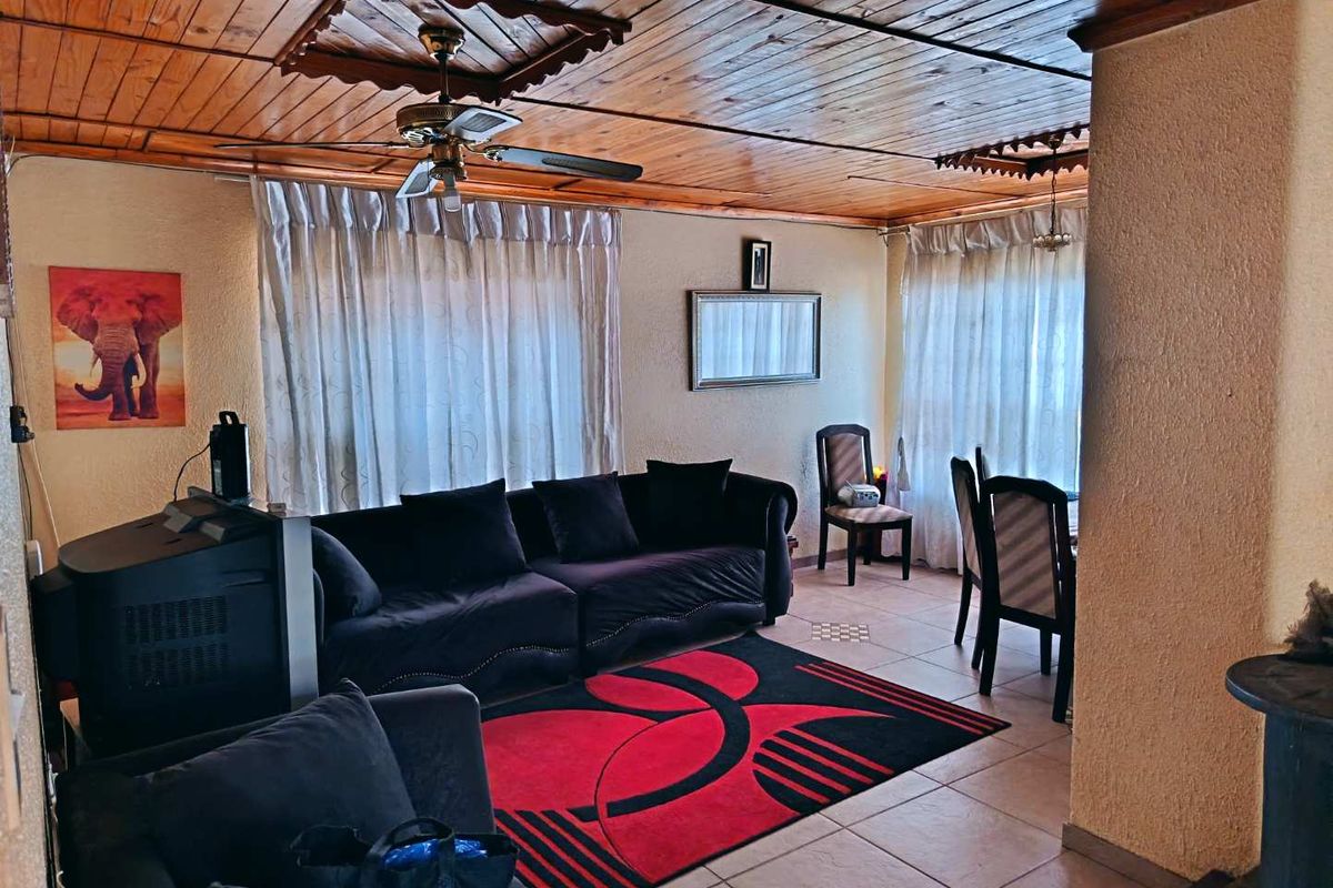 A living area featuring a distinctive timber-clad ceiling, ceiling fan, tiled flooring, and a built-in wood-burning stove.
