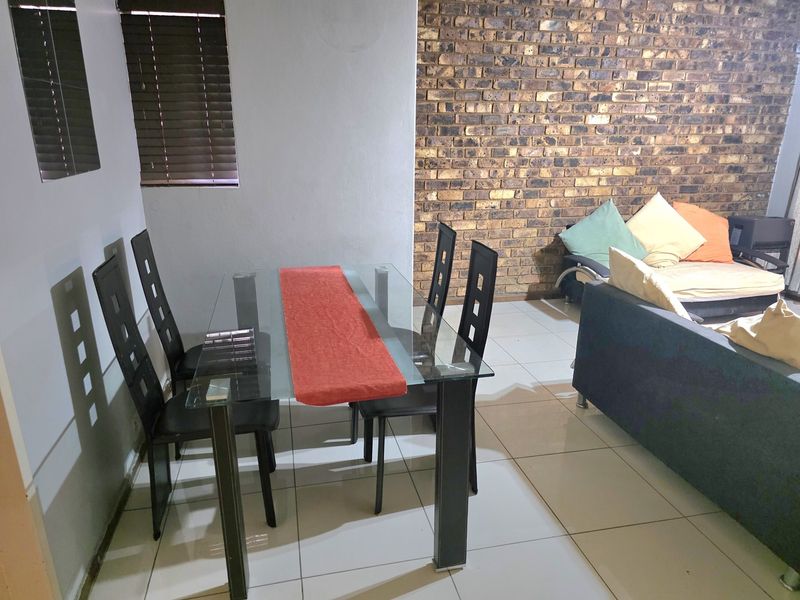 Open-plan living and dining area featuring a prominent exposed brick feature wall, neutral ceramic floor tiles, and window blinds.