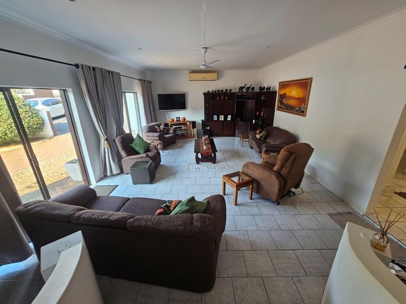 Spacious living room featuring tiled flooring, a ceiling fan, wall-mounted air conditioning, and large sliding glass doors providing access to the exterior.
