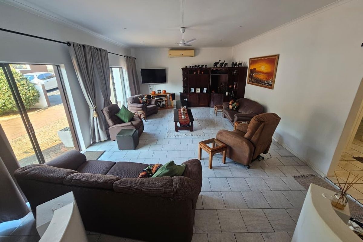 Spacious living room featuring tiled flooring, a ceiling fan, wall-mounted air conditioning, and large sliding glass doors providing access to the exterior.