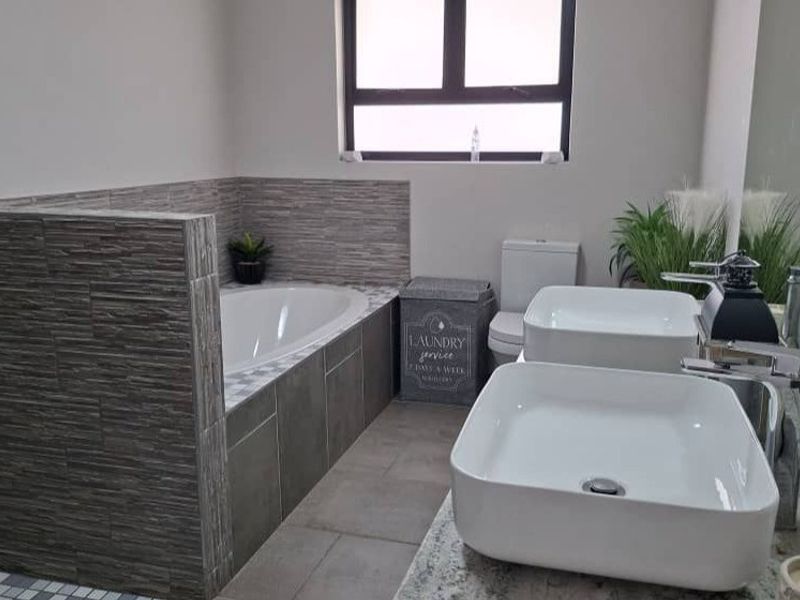 Modern bathroom featuring a built-in bathtub with textured tiling, dual vessel sinks on a granite vanity, and a neutral color palette.