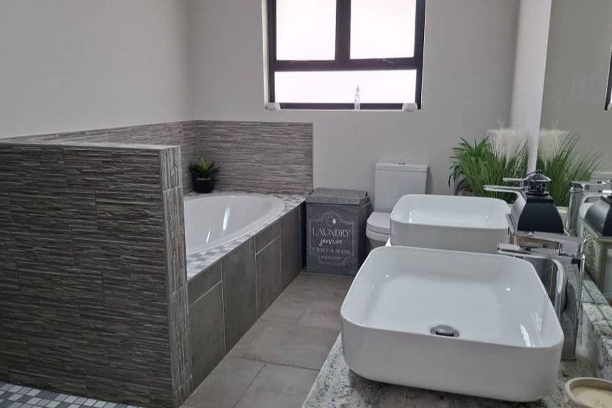 Modern bathroom featuring a built-in bathtub with textured tiling, dual vessel sinks on a granite vanity, and a neutral color palette.