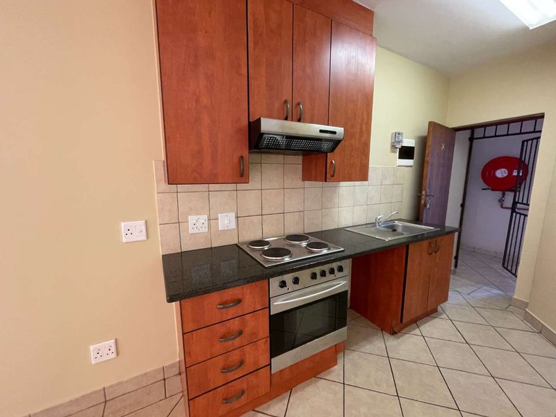 A functional kitchen featuring wood-finish cabinetry, granite countertops, a built-in electric oven and hob, and tiled flooring.