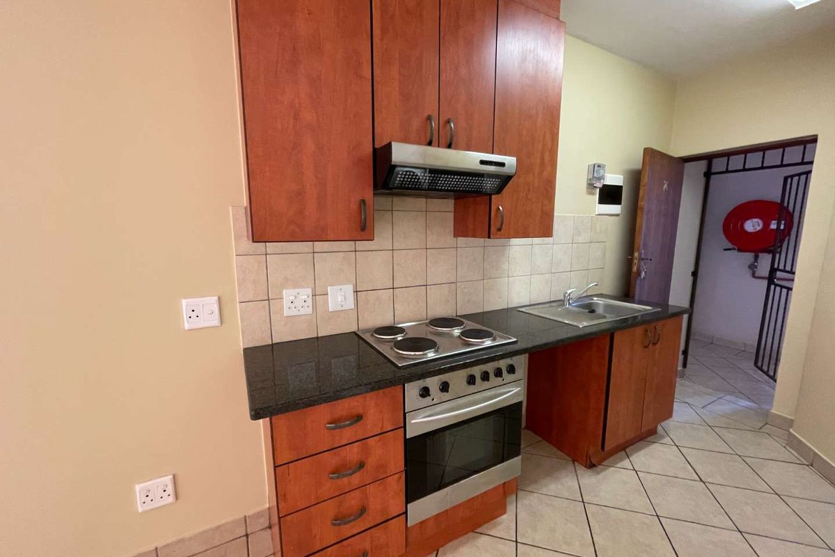 A functional kitchen featuring wood-finish cabinetry, granite countertops, a built-in electric oven and hob, and tiled flooring.