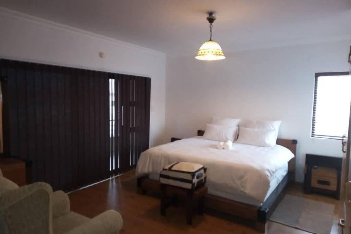 A spacious bedroom featuring laminate flooring, large sliding doors with vertical blinds, and a built-in fireplace.