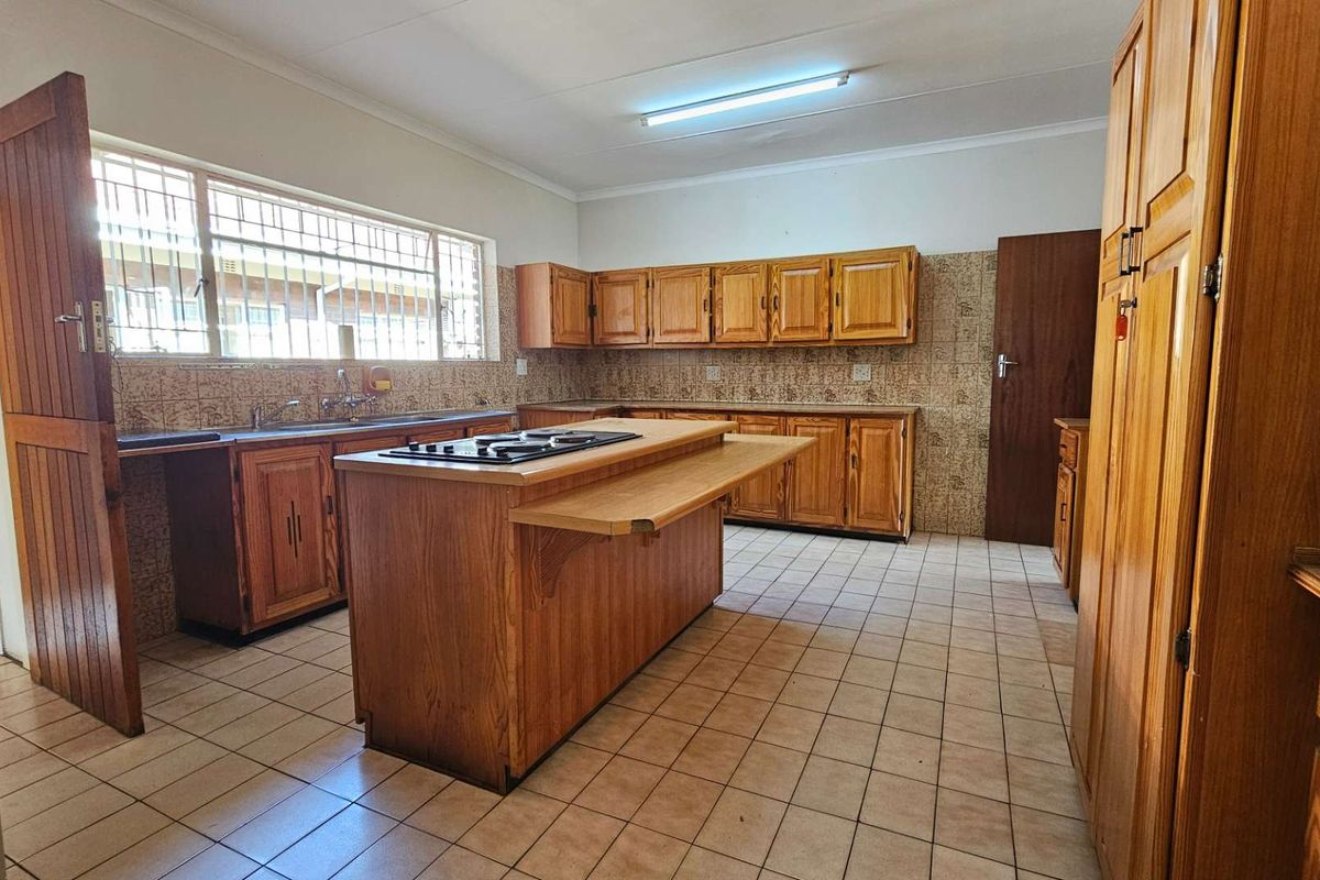Spacious kitchen featuring solid wood cabinetry, a central island with a built-in hob, and tiled flooring throughout.