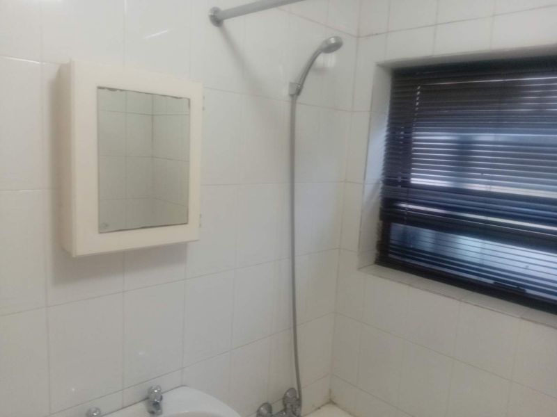 A functional bathroom featuring tiled walls, a wall-mounted medicine cabinet, and a shower fixture, requiring cosmetic updates to modernize the space.