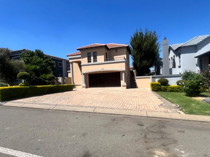 A well-maintained double-story residential property featuring a paved driveway, double garage, and landscaped front garden under a clear blue sky.