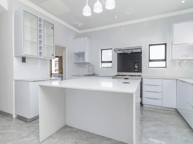 Modern, bright kitchen featuring a central island, white cabinetry, quartz countertops, and high-quality tiled flooring, offering a clean and functional culinary space.