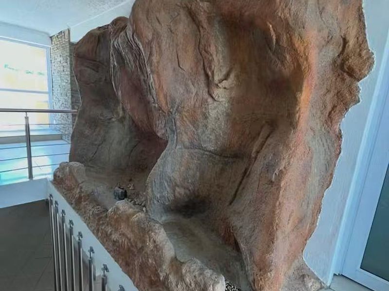 A hallway area featuring a prominent decorative rock feature alongside a staircase with a modern stainless steel balustrade and tiled flooring.