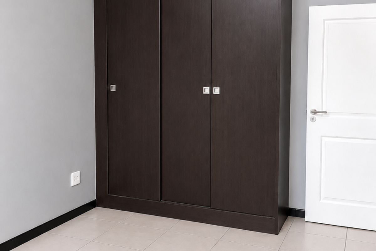 A clean, empty bedroom featuring neutral grey walls, light-colored floor tiles, and a dark wood built-in wardrobe.