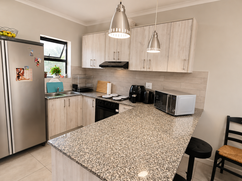 A functional kitchen featuring light wood-look cabinetry, granite countertops, a tiled backsplash, and modern pendant lighting, providing a clean and practical workspace.
