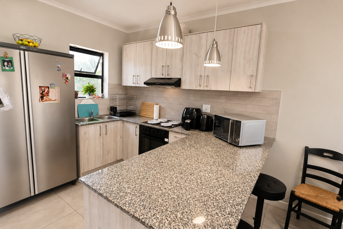 A functional kitchen featuring light wood-look cabinetry, granite countertops, a tiled backsplash, and modern pendant lighting, providing a clean and practical workspace.