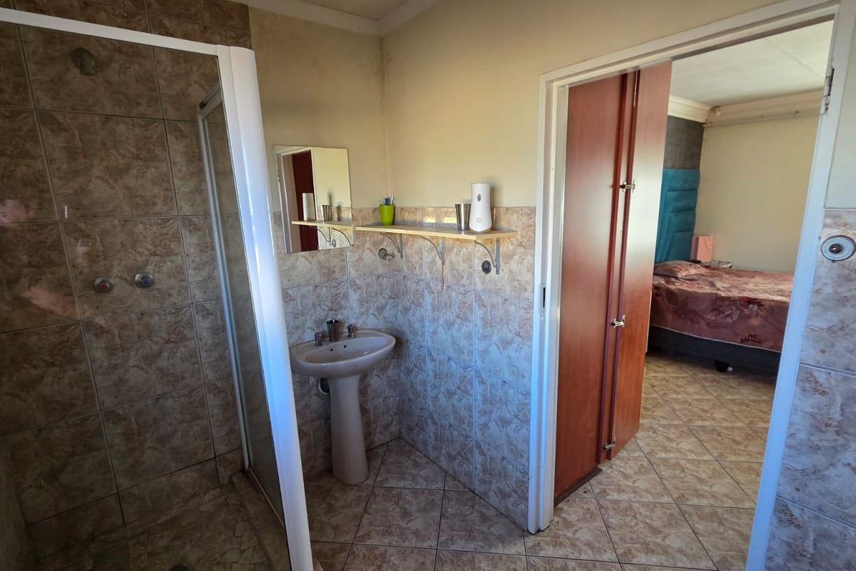 A functional bathroom featuring a shower enclosure, pedestal basin, and tiled finishes, with direct access to an adjacent bedroom.