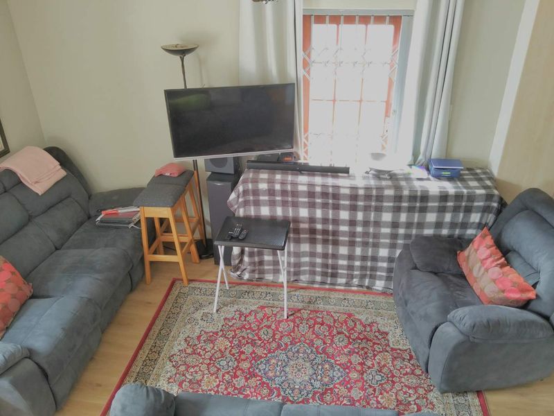 A living room area featuring laminate flooring and a window with a security gate, providing a functional space for relaxation.