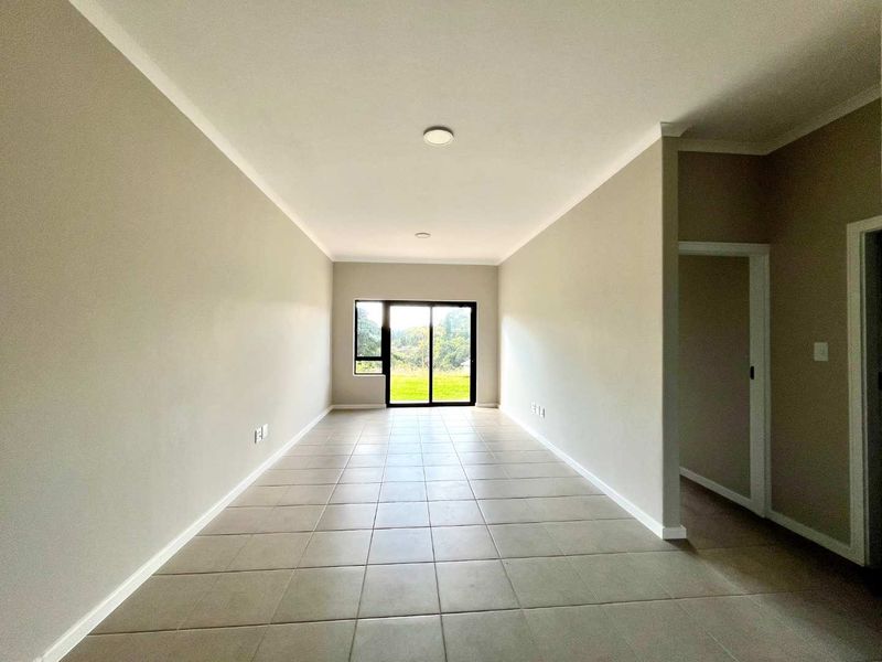 A bright, empty living area featuring neutral wall tones, tiled flooring, and a sliding glass door providing natural light and outdoor access.