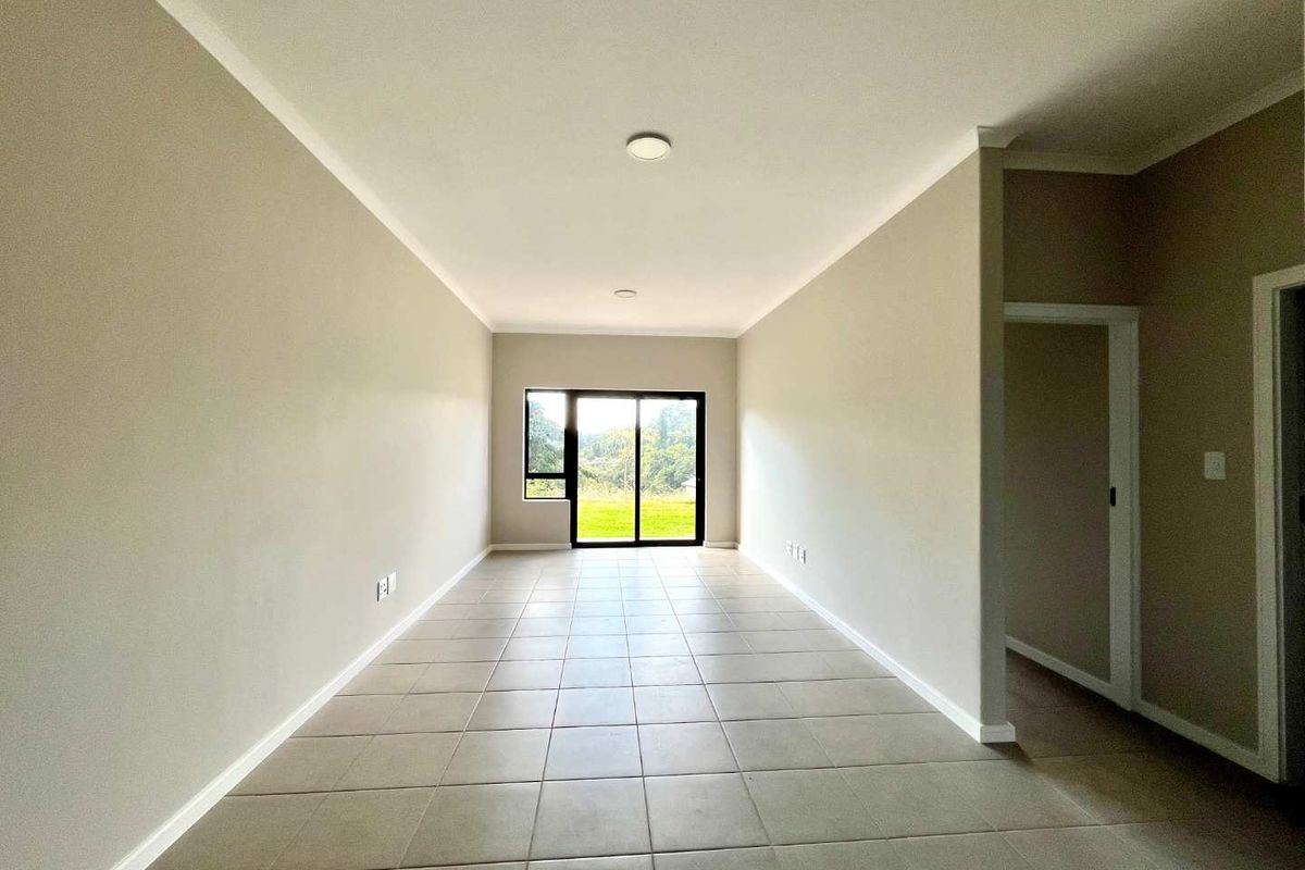 A bright, empty living area featuring neutral wall tones, tiled flooring, and a sliding glass door providing natural light and outdoor access.