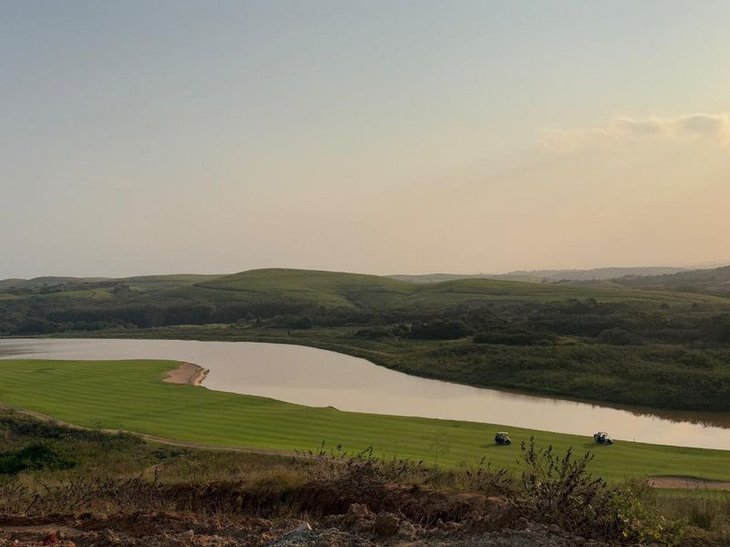 A scenic elevated view overlooking a golf course fairway and a large lake, surrounded by rolling green hills.