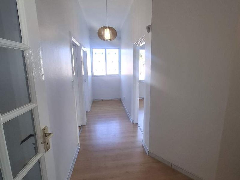 A bright, empty hallway featuring light-toned laminate flooring, a ceiling access hatch, and a central pendant light fixture.