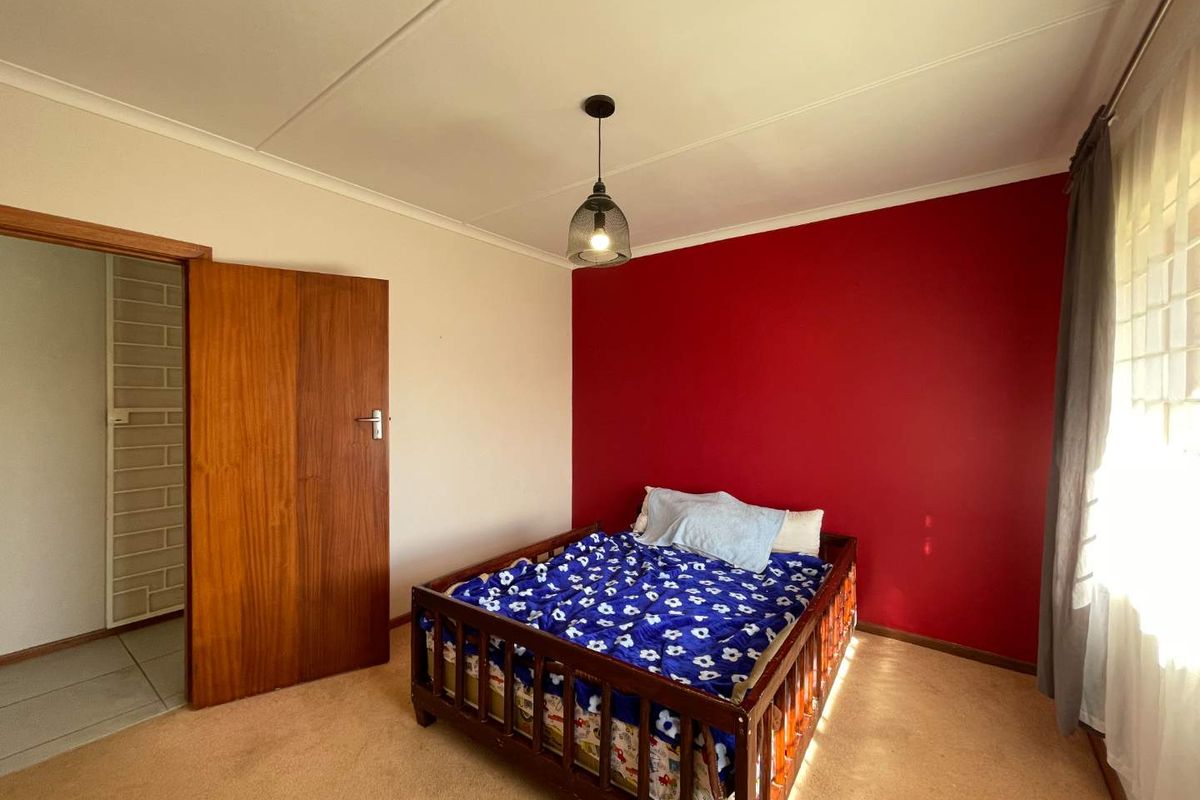 A bedroom featuring carpeted flooring, a pendant light fixture, and a bold red accent wall.