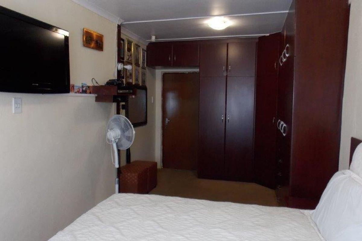 A functional bedroom featuring built-in wooden cupboards with overhead storage and neutral wall finishes.