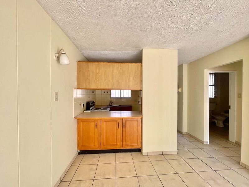A compact, dated kitchen featuring laminate cabinetry, an electric stove, and ceramic floor tiles, offering a functional layout ready for modernization.