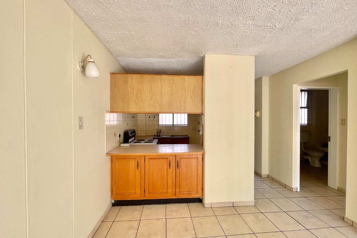 A compact, dated kitchen featuring laminate cabinetry, an electric stove, and ceramic floor tiles, offering a functional layout ready for modernization.