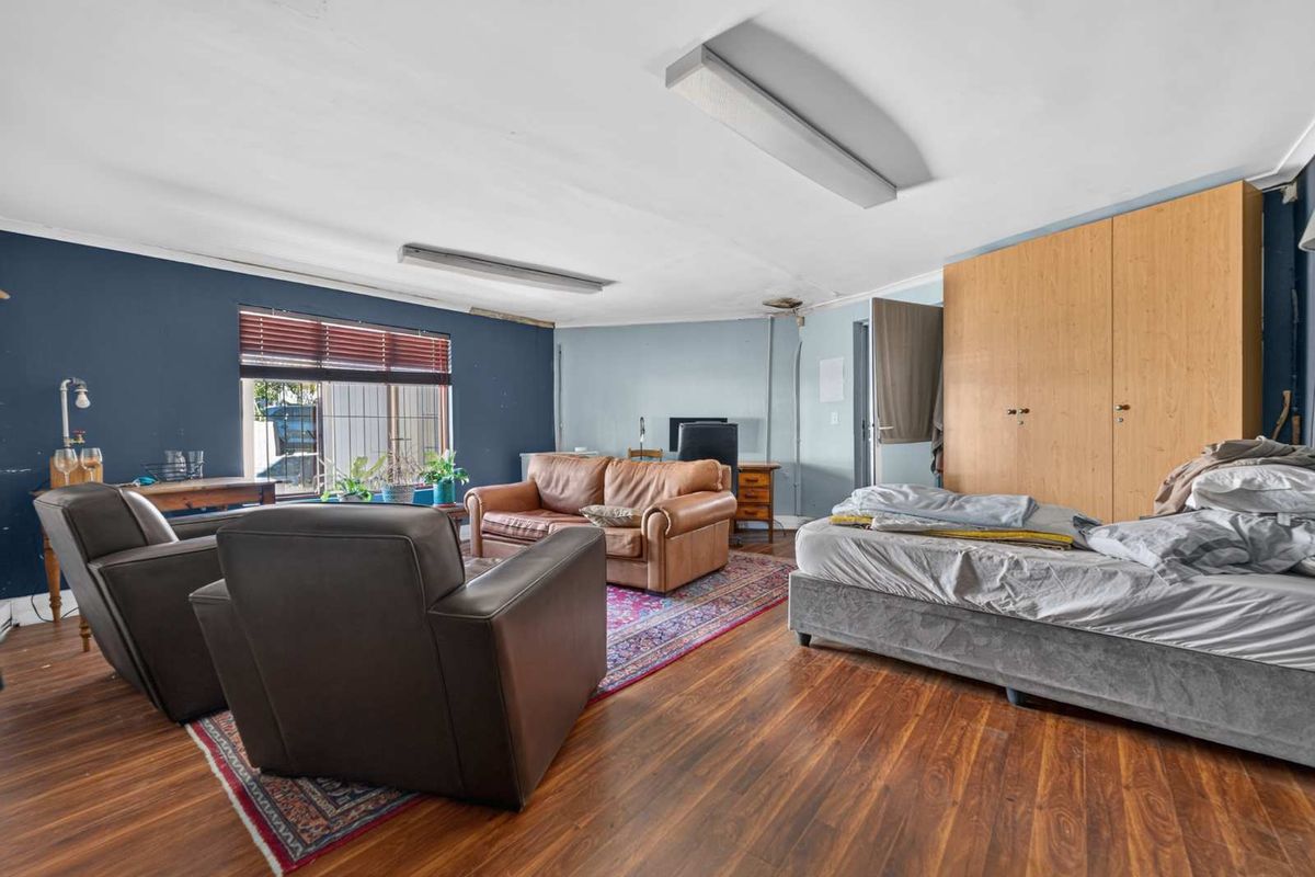 Spacious bedroom featuring laminate flooring, built-in wardrobe storage, and large windows with venetian blinds, requiring some cosmetic updates to the ceiling and walls.