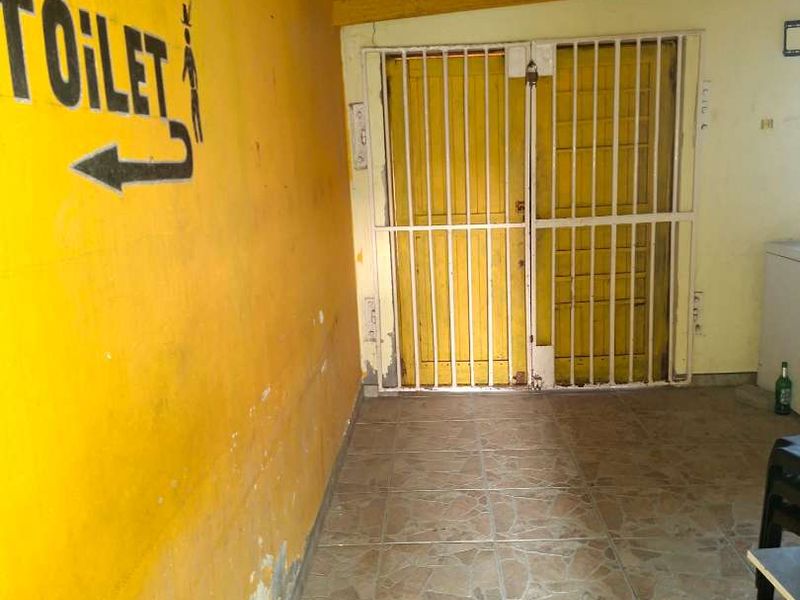 A covered outdoor patio area featuring tiled flooring, exposed timber rafters, and a security gate, currently showing signs of wear and peeling paint.