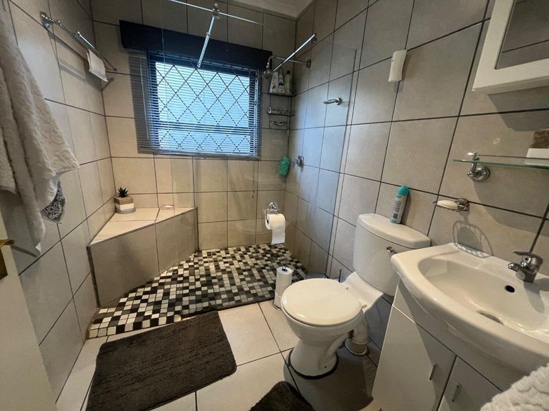 A functional bathroom featuring a walk-in shower with a built-in corner seat, tiled finishes, a vanity basin, and a standard toilet.