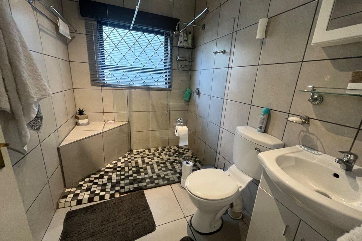A functional bathroom featuring a walk-in shower with a built-in corner seat, tiled finishes, a vanity basin, and a standard toilet.