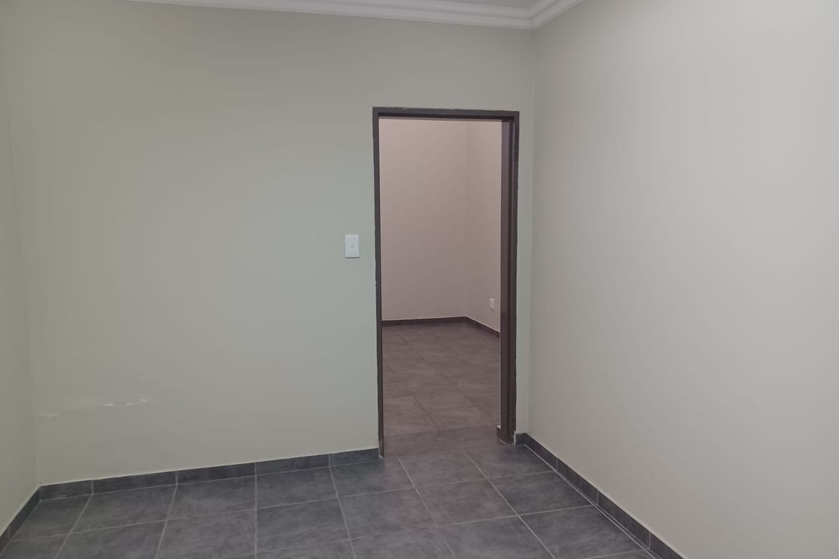 An empty room featuring grey tiled flooring, neutral painted walls, and a doorway leading to an adjacent space.